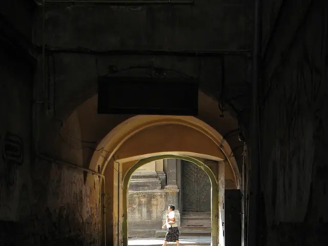 In the image we can see an arch and the footpath. Here we can see a person walking and wearing...
