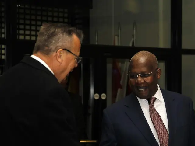 In this picture there are two people standing and talking. At the back there flags behind the glass...