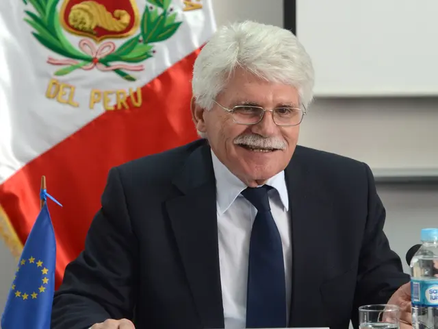 A room. There is a flag on the top which consists of del peru name. There is a person sitting, he...